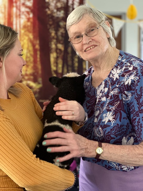 A carer holding the black and white lamb whilst a female resident strokes it