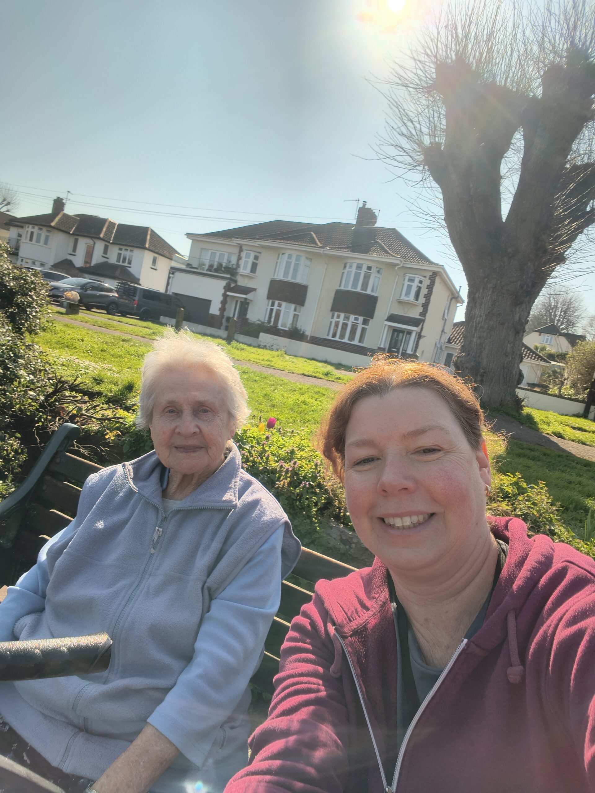 Resident and carer sitting on a bench in the park taking a selfie
