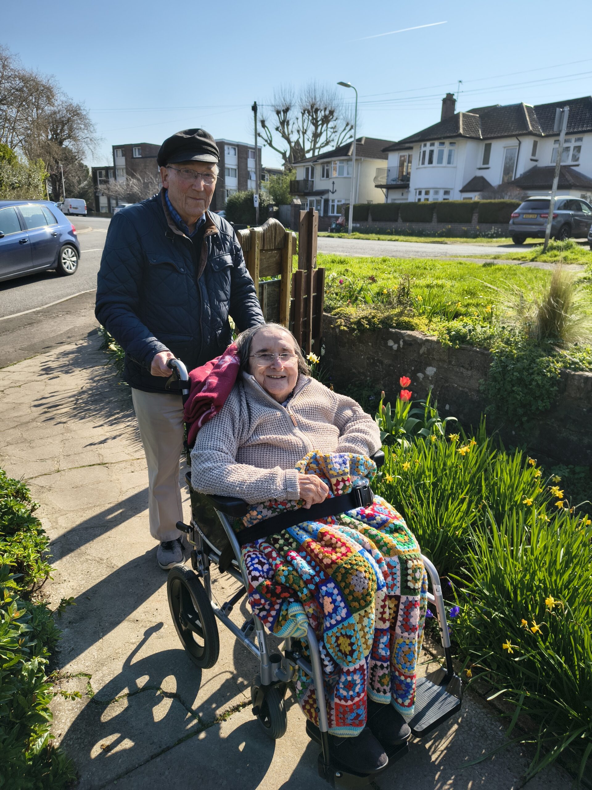 Residents, one pushing a wheelchair with resident in a park