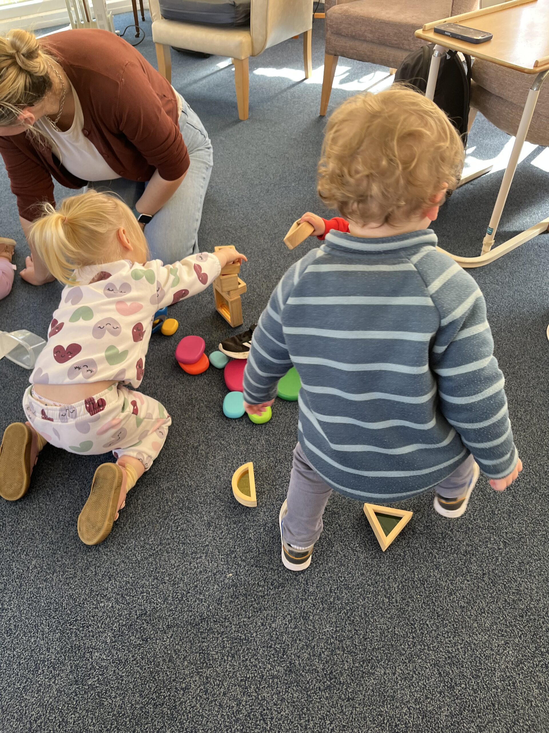 Toddlers playing on the floor with wooden shapes scaled