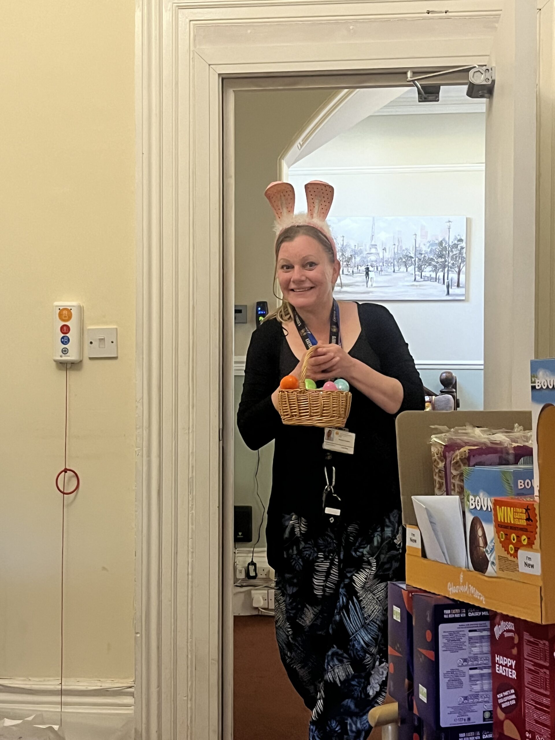 Carer Gemma dressed in bunny ears holding a basket of colourful plastic eggs