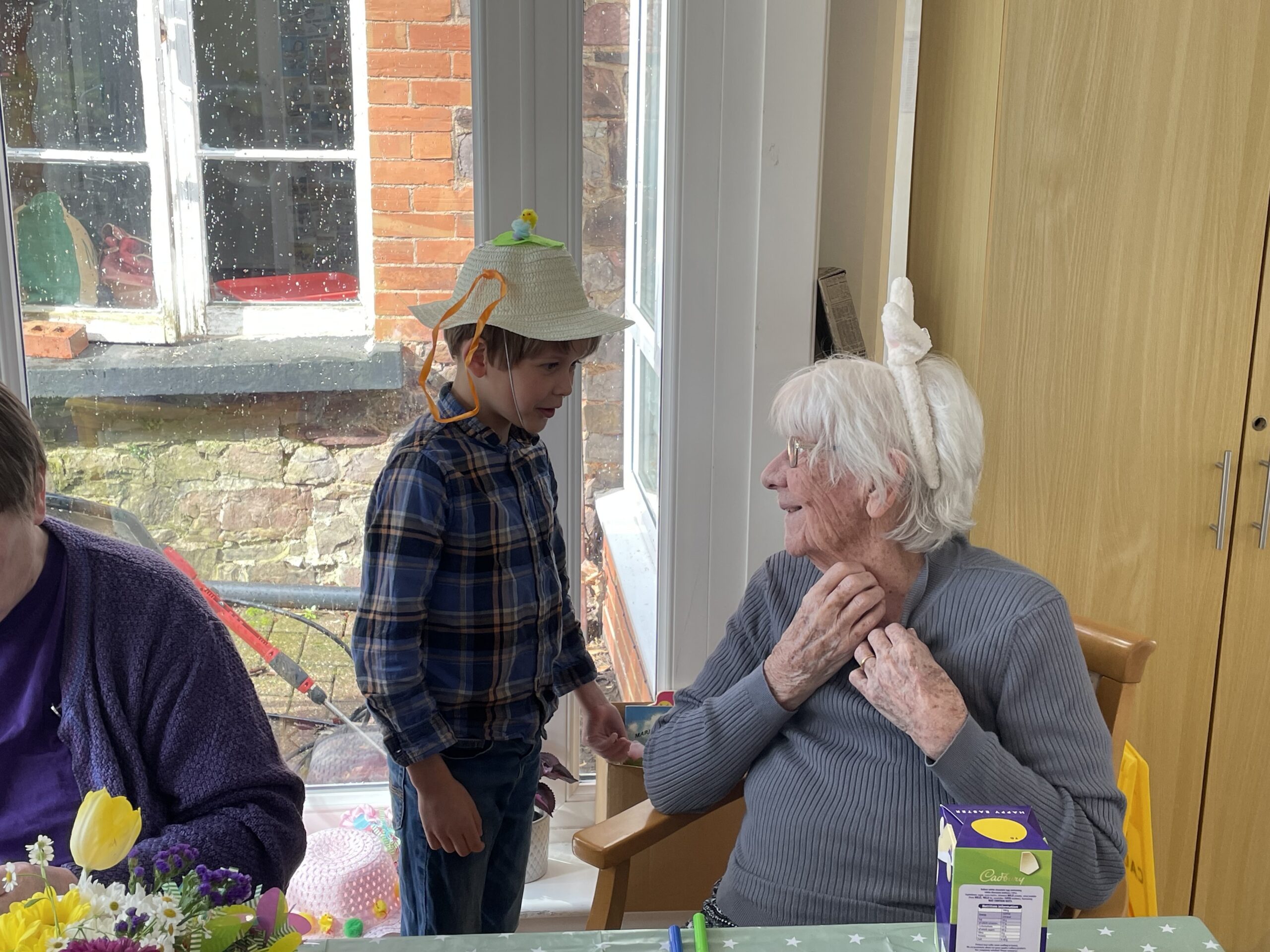 Child wearing decorated Easter bonnet talking to a resident wearing white bunny ears hairband scaled