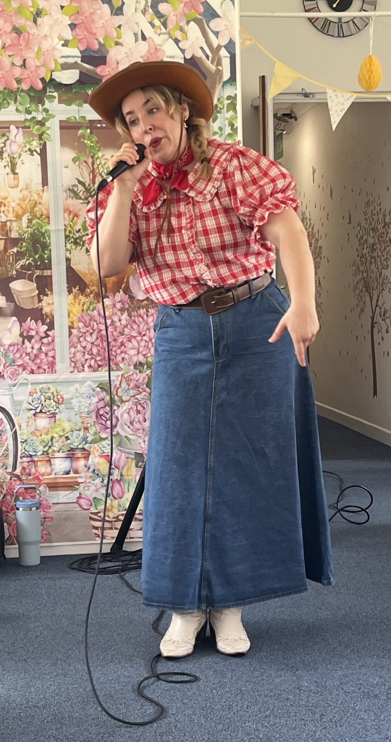 Dolly singing dressed in a cowgirl hat, red and white check shirt and long denim skirt.