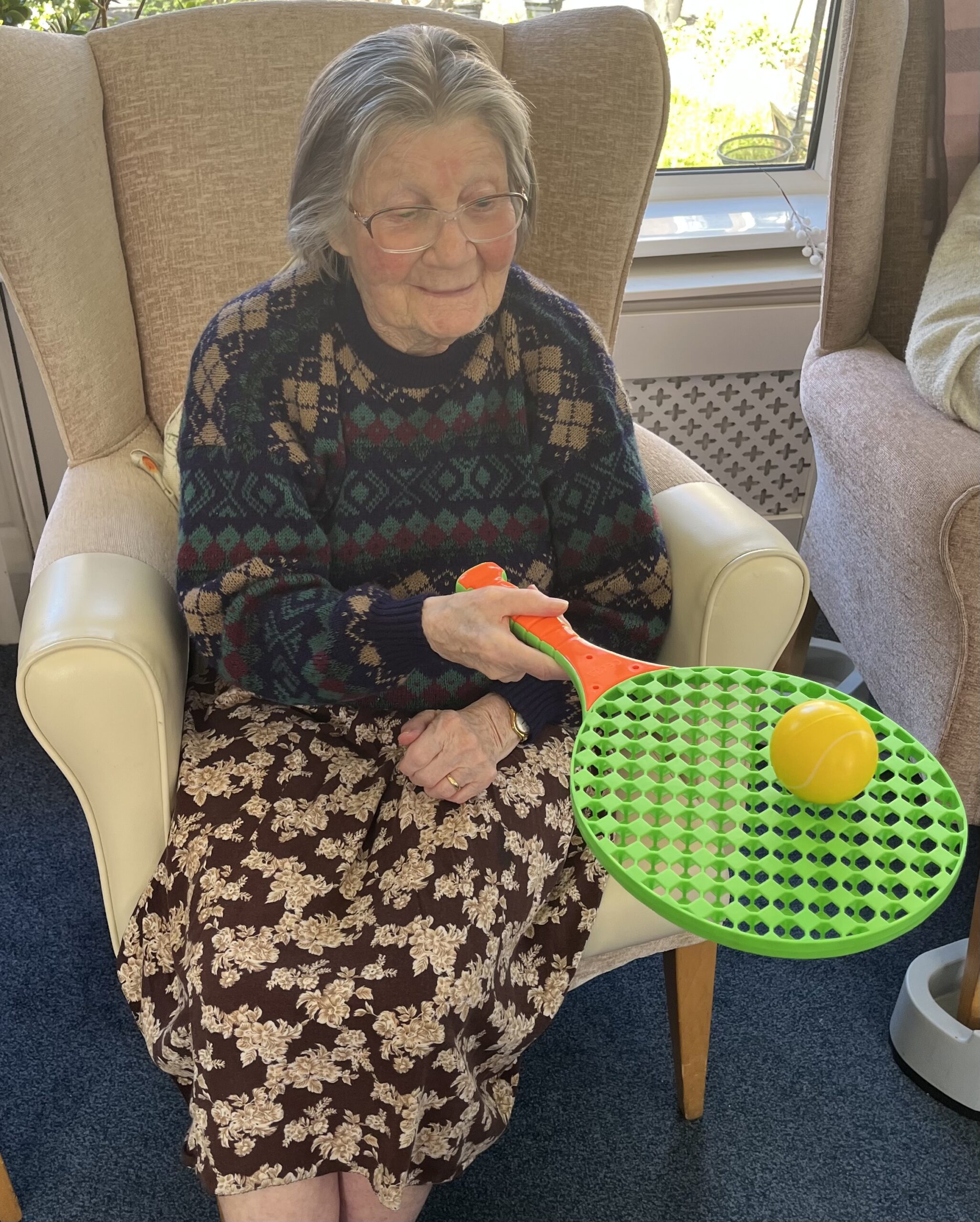 Eileen balancing a tennis ball on a racket whilst seated scaled