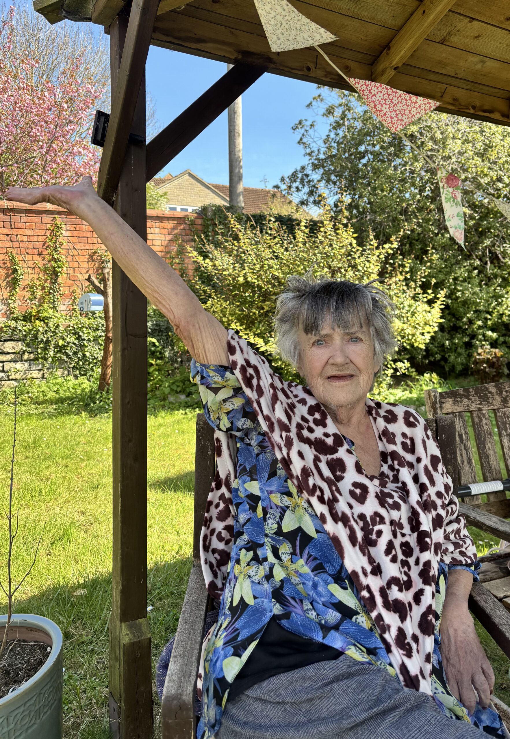 Female resident sat outside in the garden under the gazebo arm lifted to the sky scaled