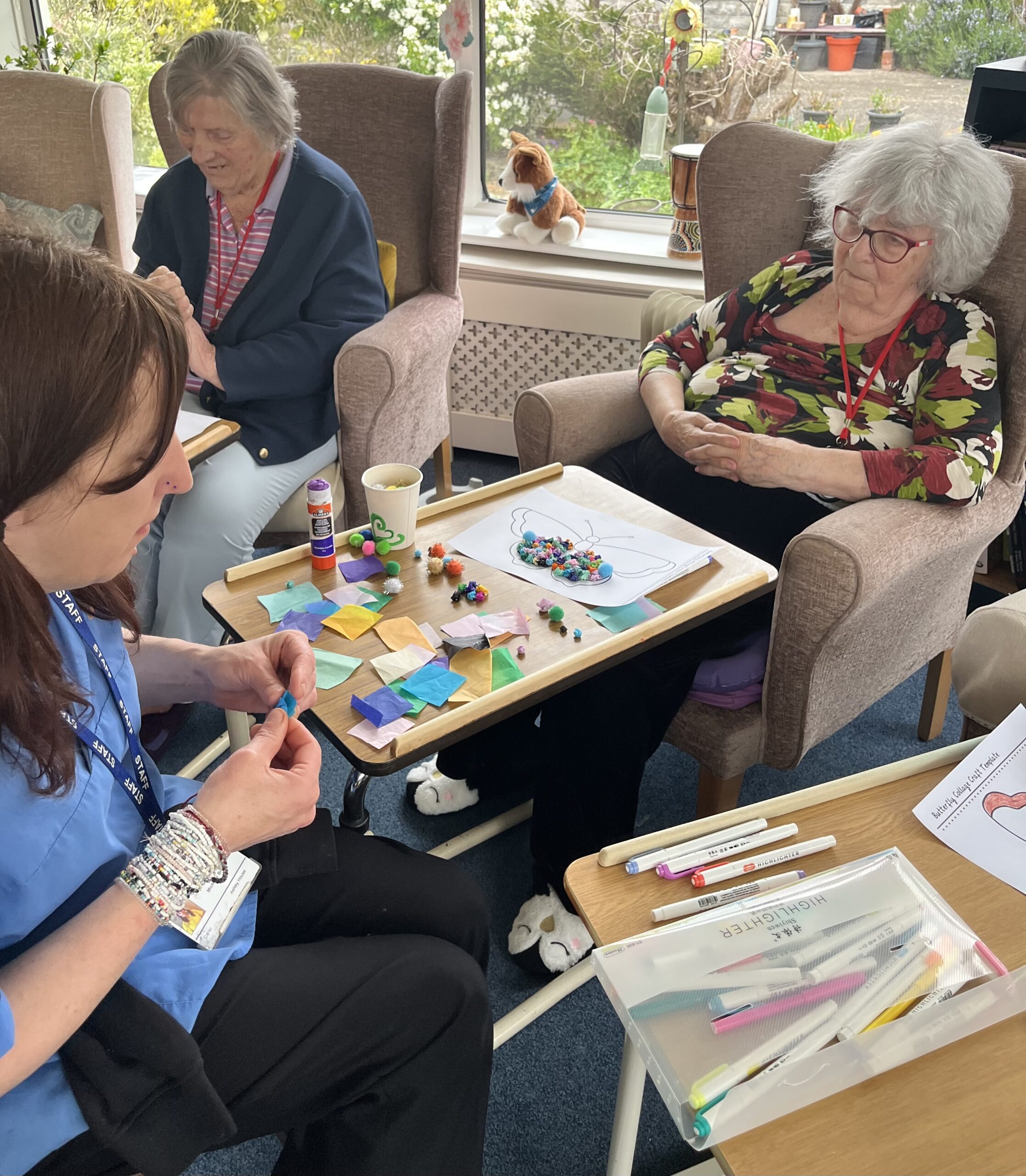 Maggie and a carer working together making tissue paper balls to stick on her butterfly