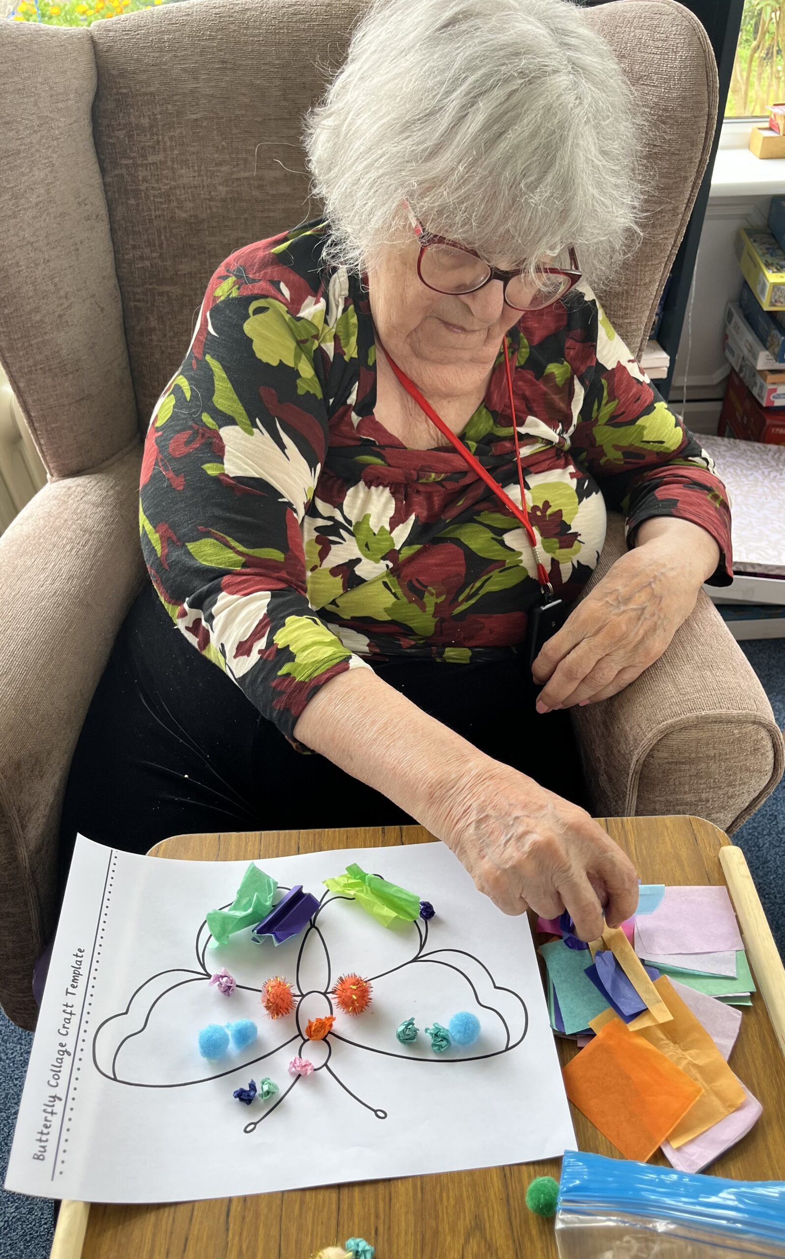 Maggie and a carer working together making tissue paper balls to stick on her butterfly