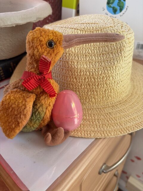 Pink egg hidden between a straw hat and a soft toy kiwi bird