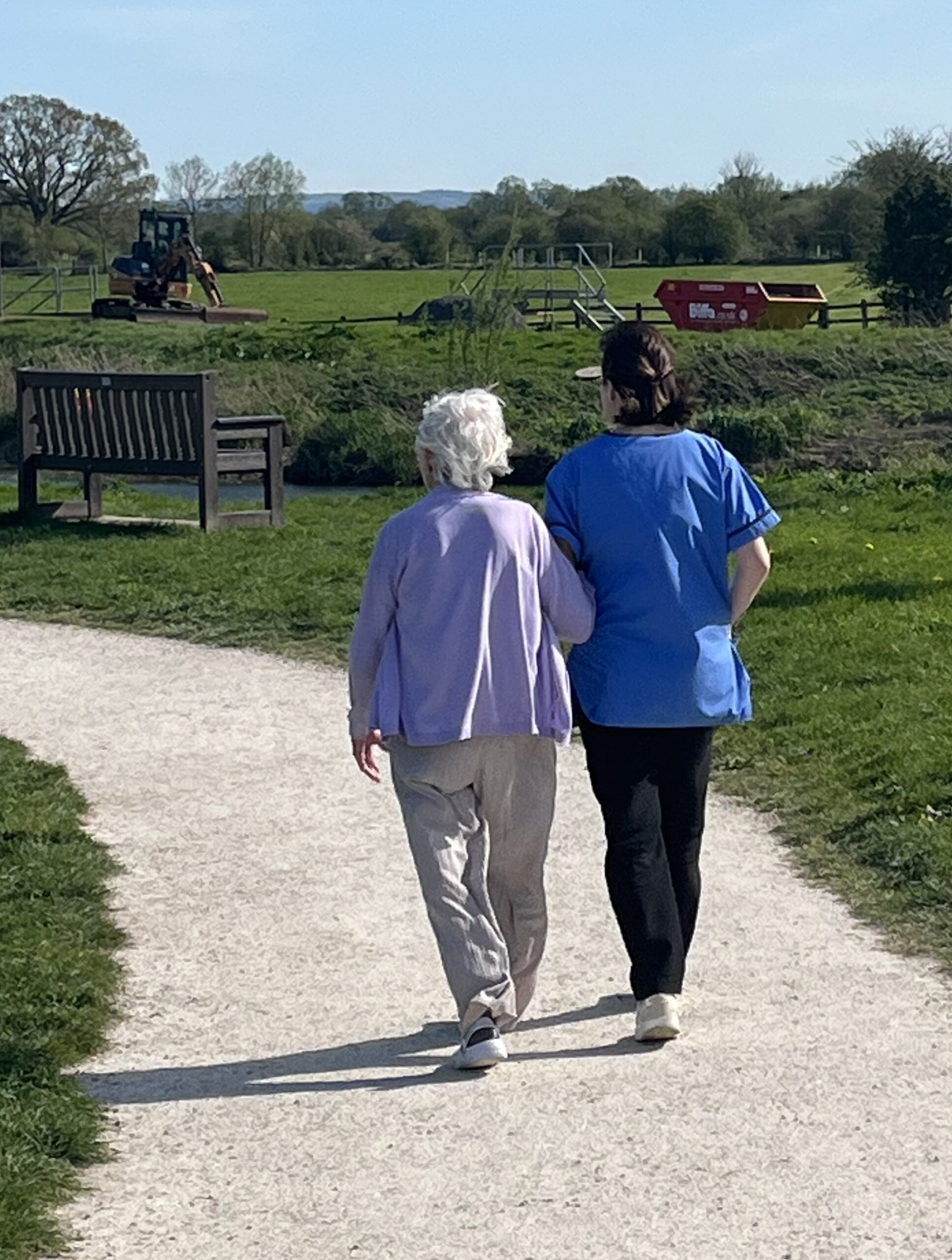 Resident and carer walking in the sunshine beside the river scaled