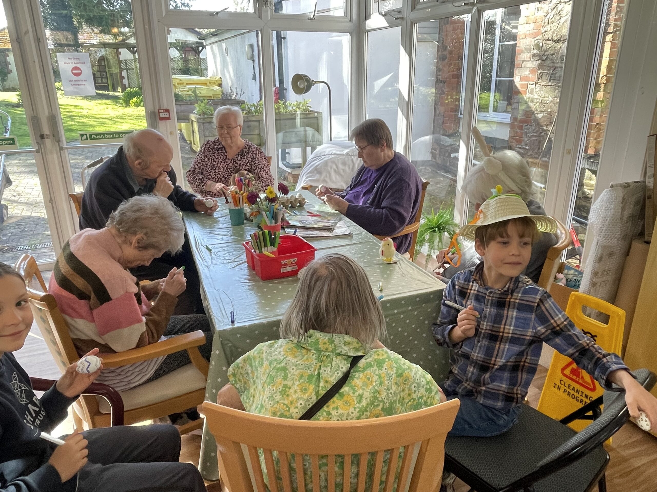 Residents and children seated around a table decorating eggs with felt tip pens scaled