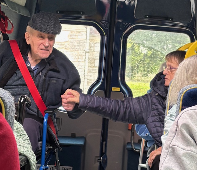 Residents in the back of the minibus holding hands in comfort