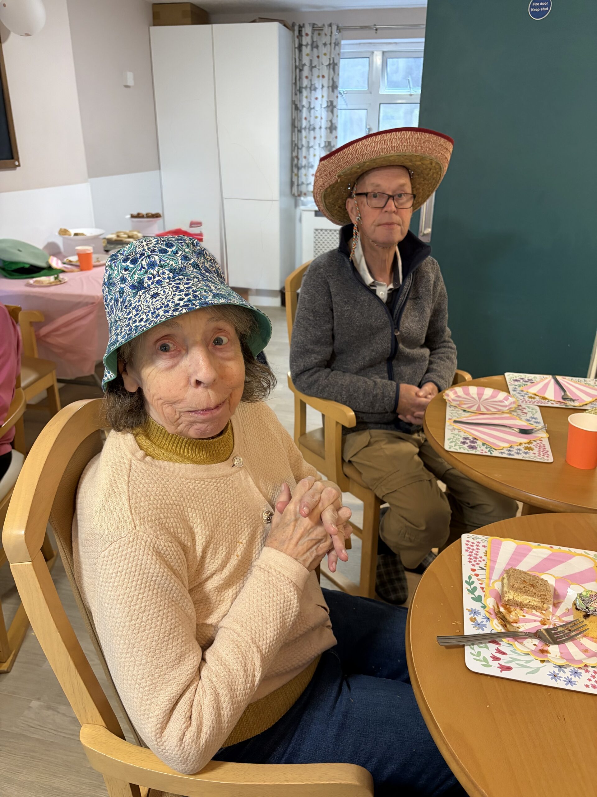 Residents seated around a table enjoying the party food wearing hats