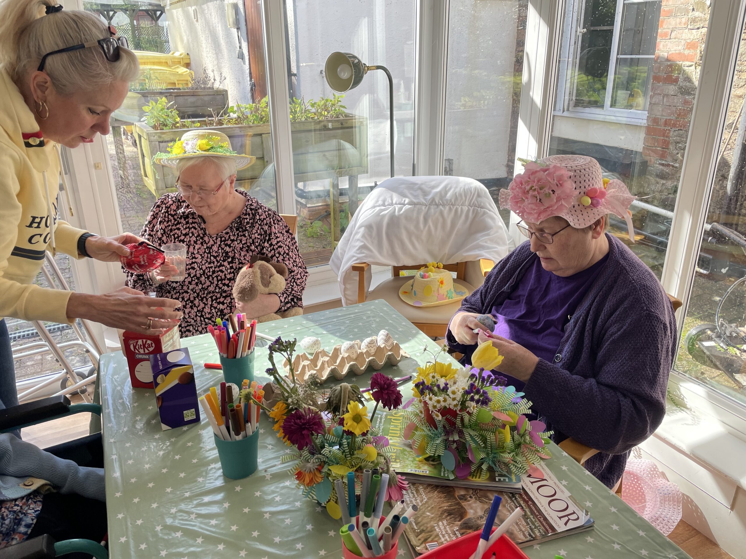 Residents seated around a table flower arranging while wearing Easter bonnets scaled
