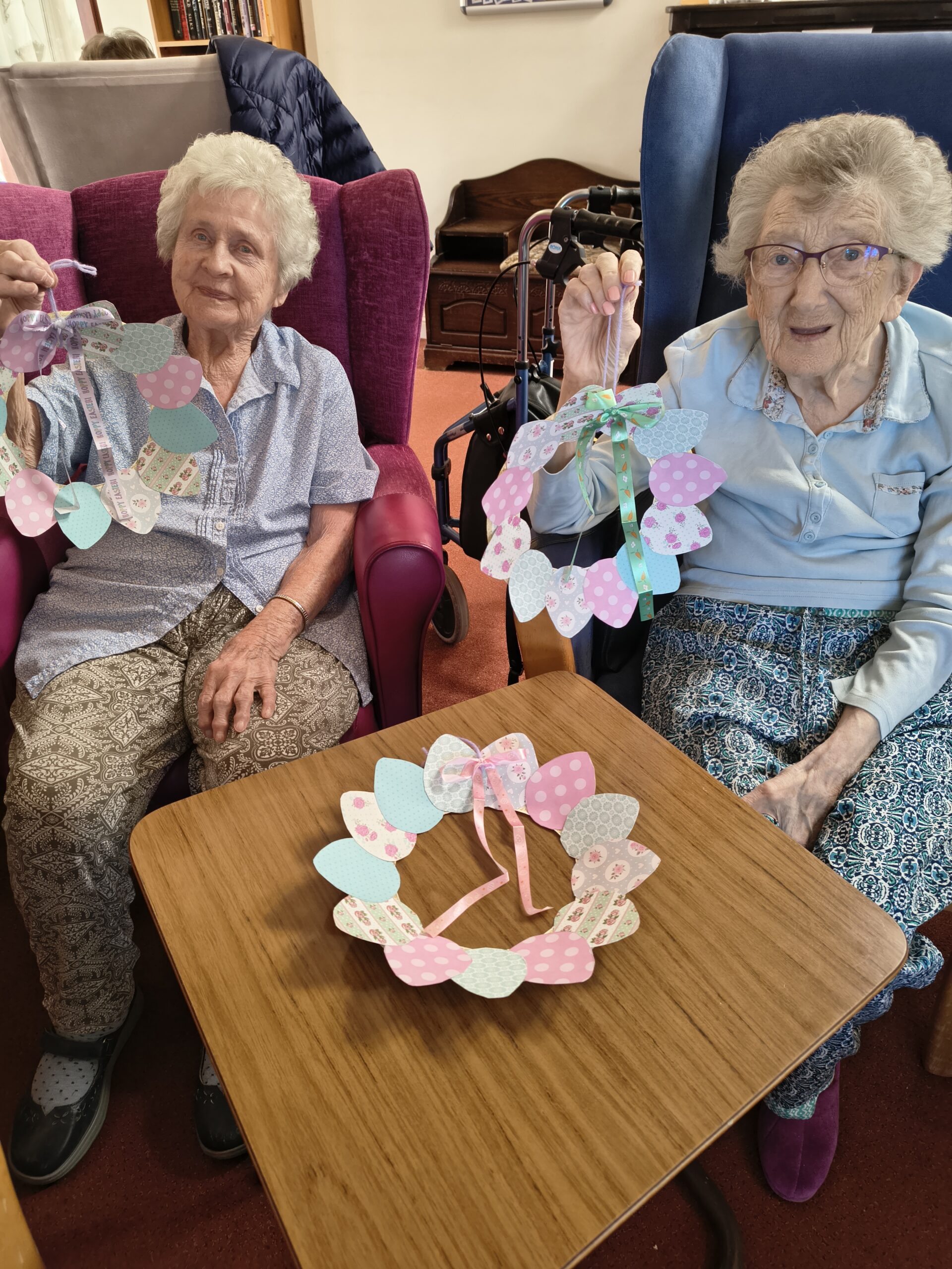 Two female residents holding up their finished wreaths scaled