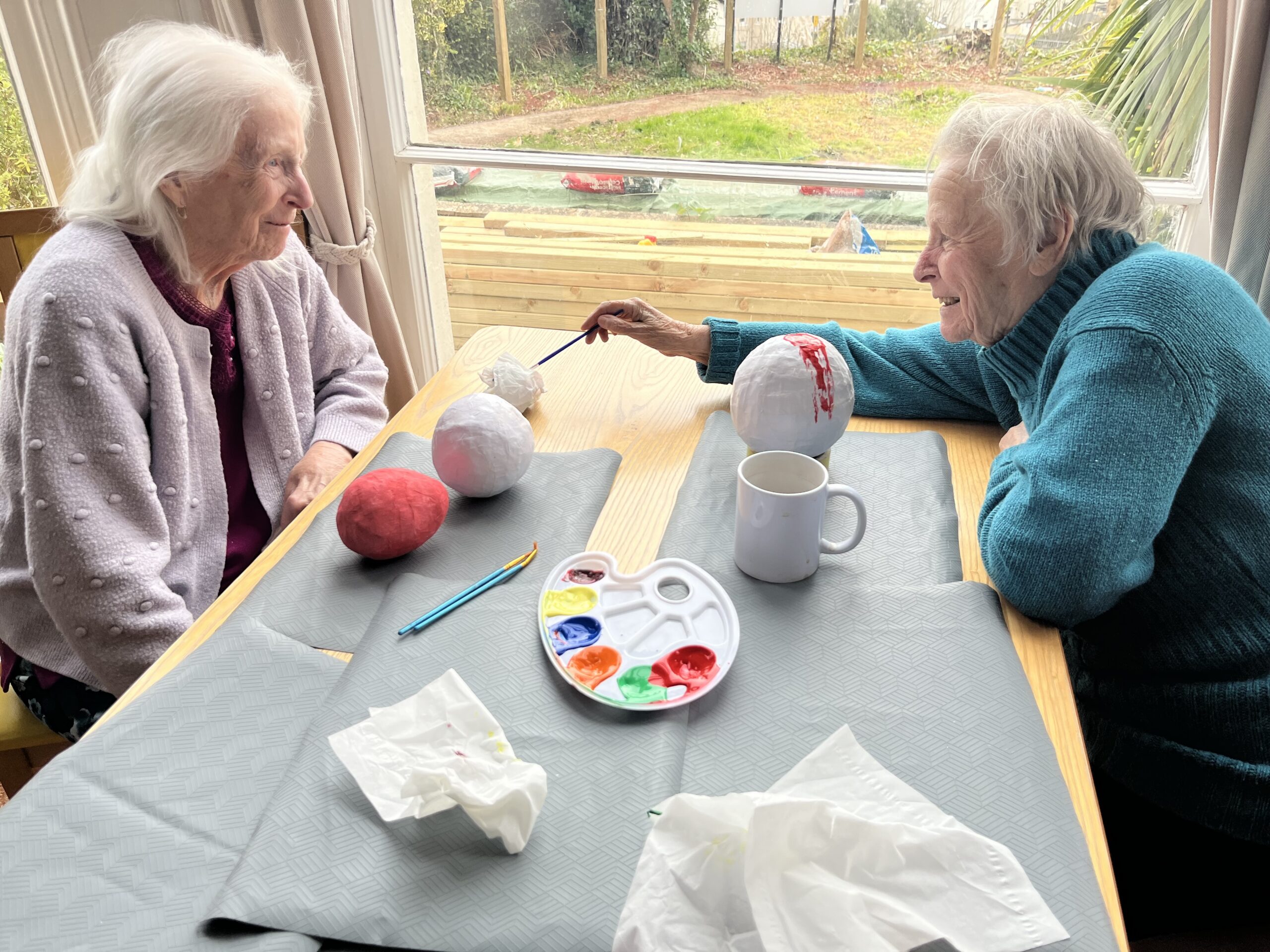 Two female residents painting their Easter eggs with chat and a cup of tea