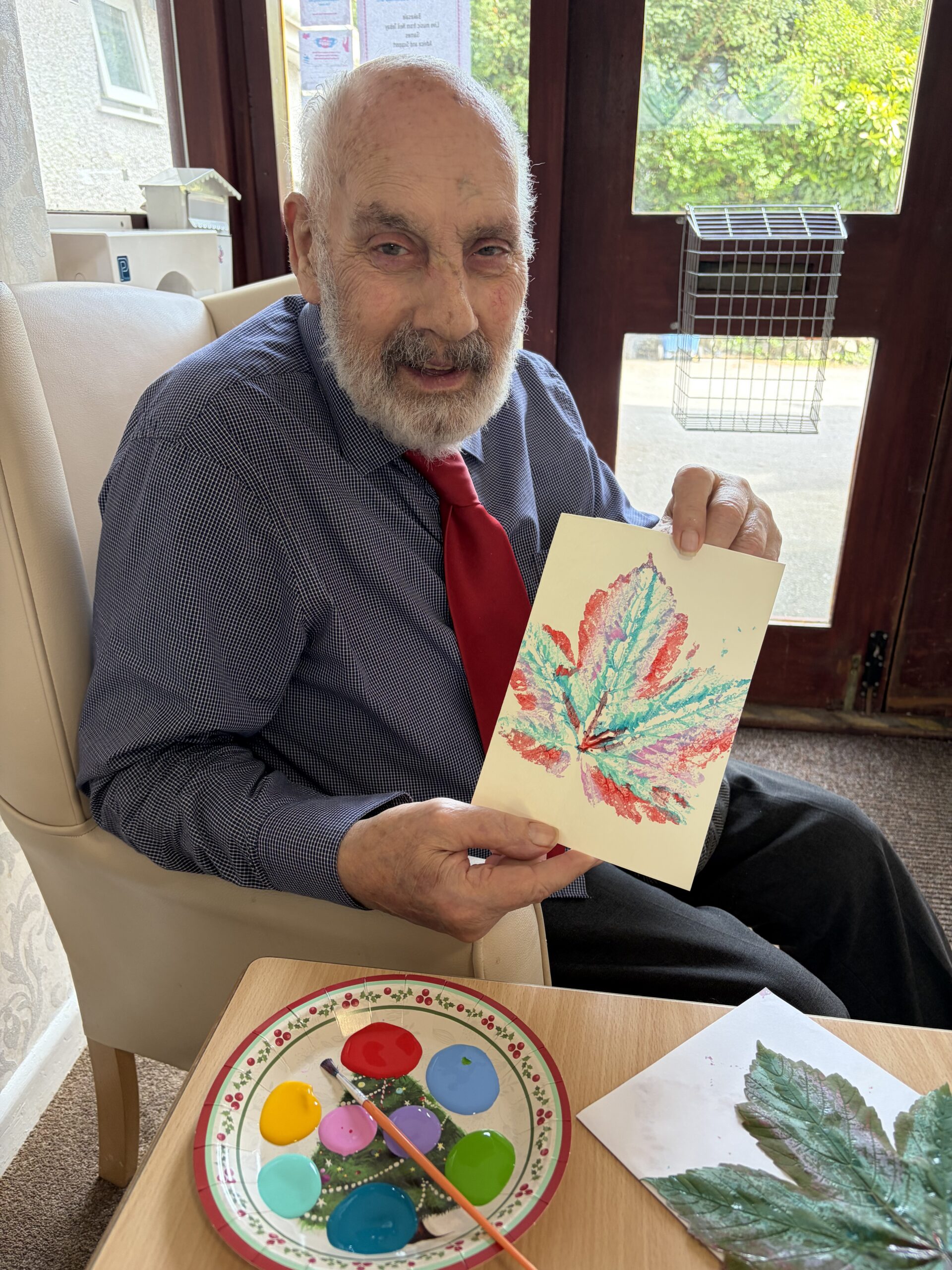A male resident proudly holding up his finished artwork of a leaf in different coloured paints