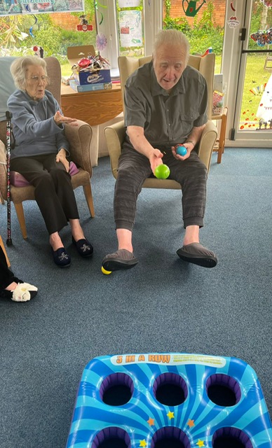Bill seated throwing a ball at a 3x3 hole blow-up mat