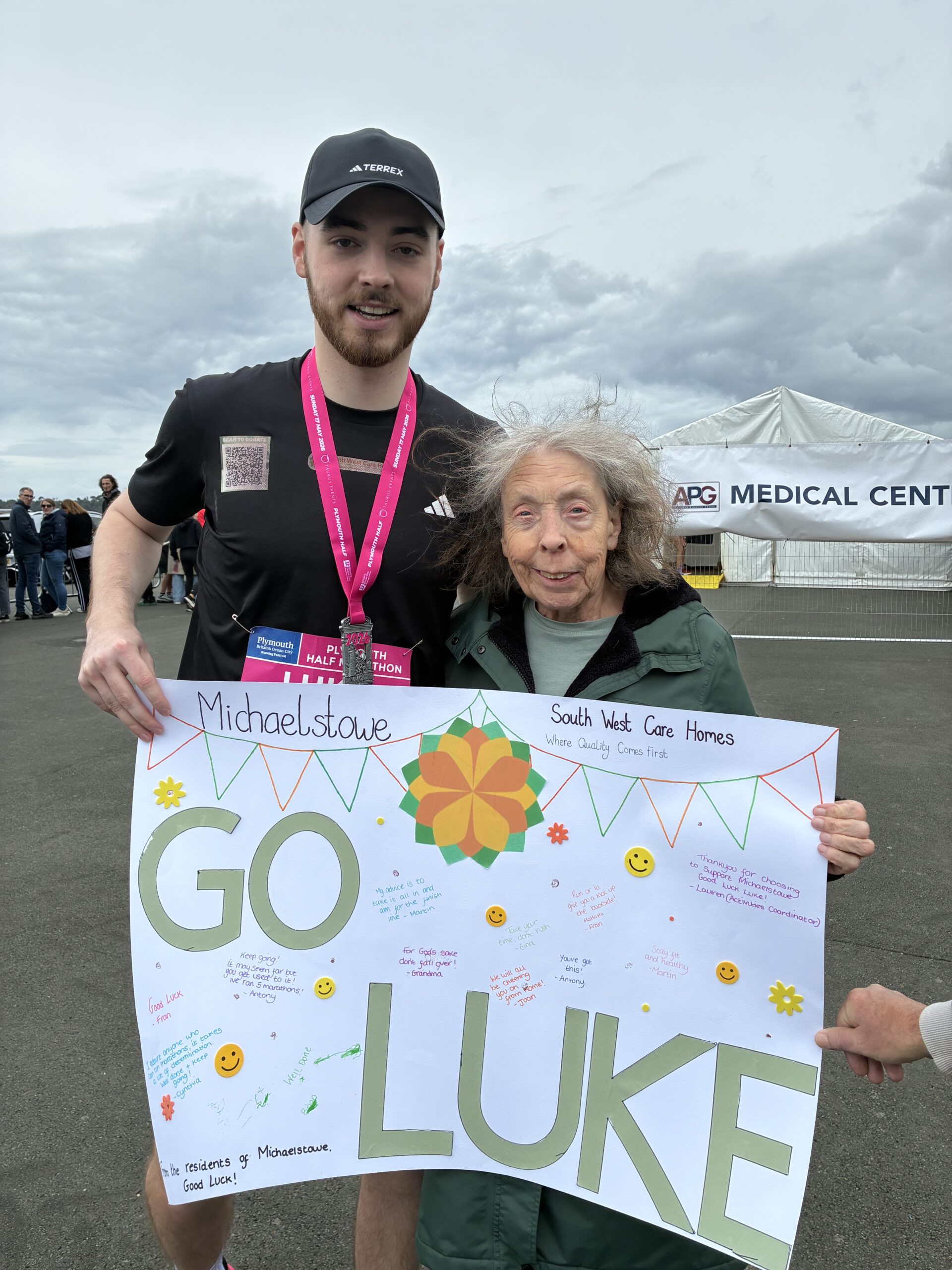 Carol holding her sign with Luke beside her wearing his completion medal