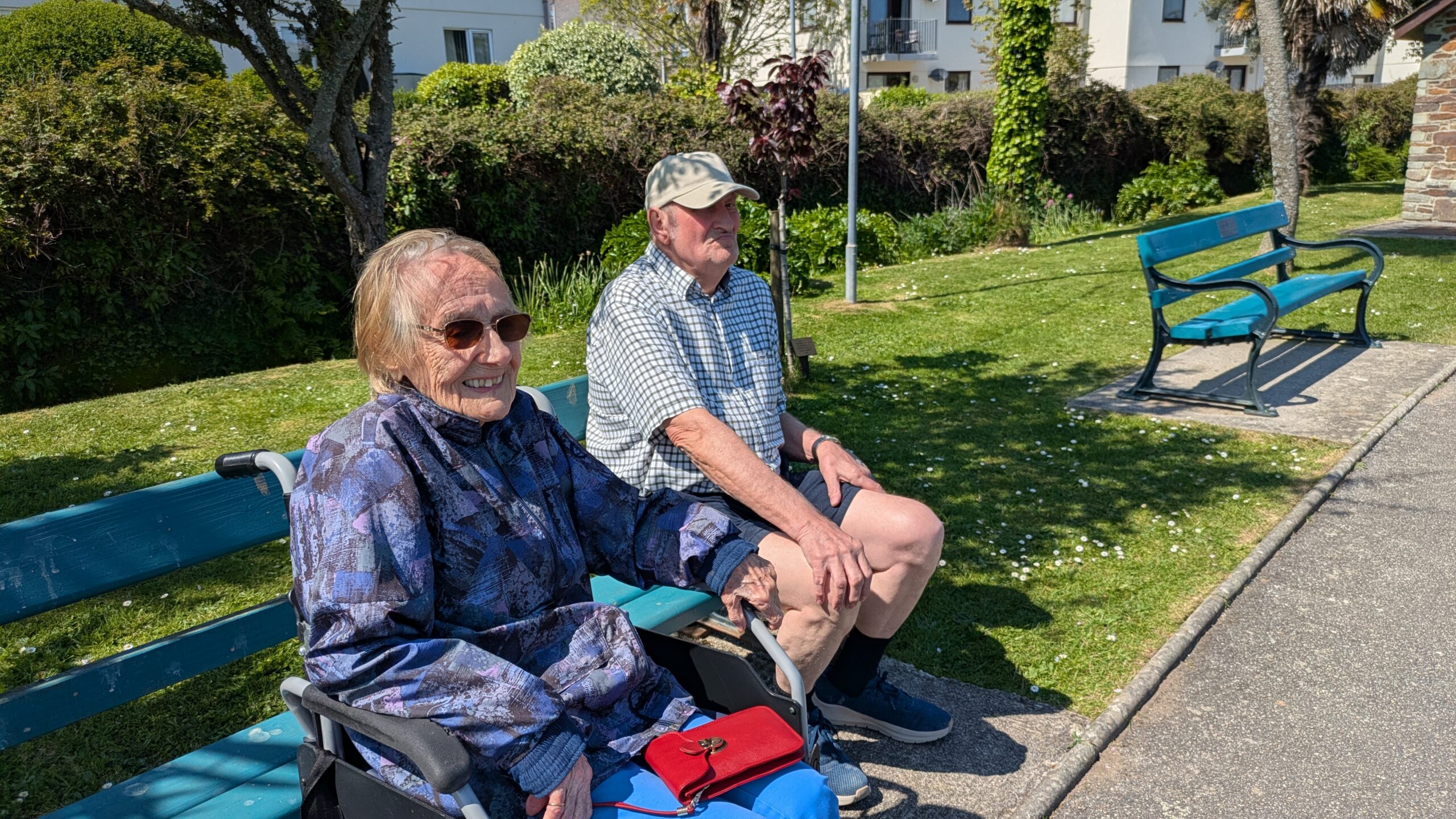 Cecily in her wheelchair and Dave seated on a bench in a park