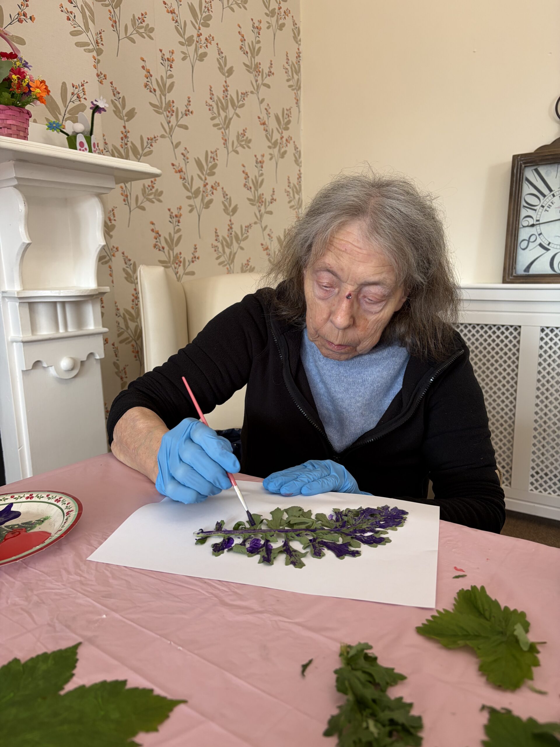 Female resident seated at a table painting leaves and using them as stamps to create a picture
