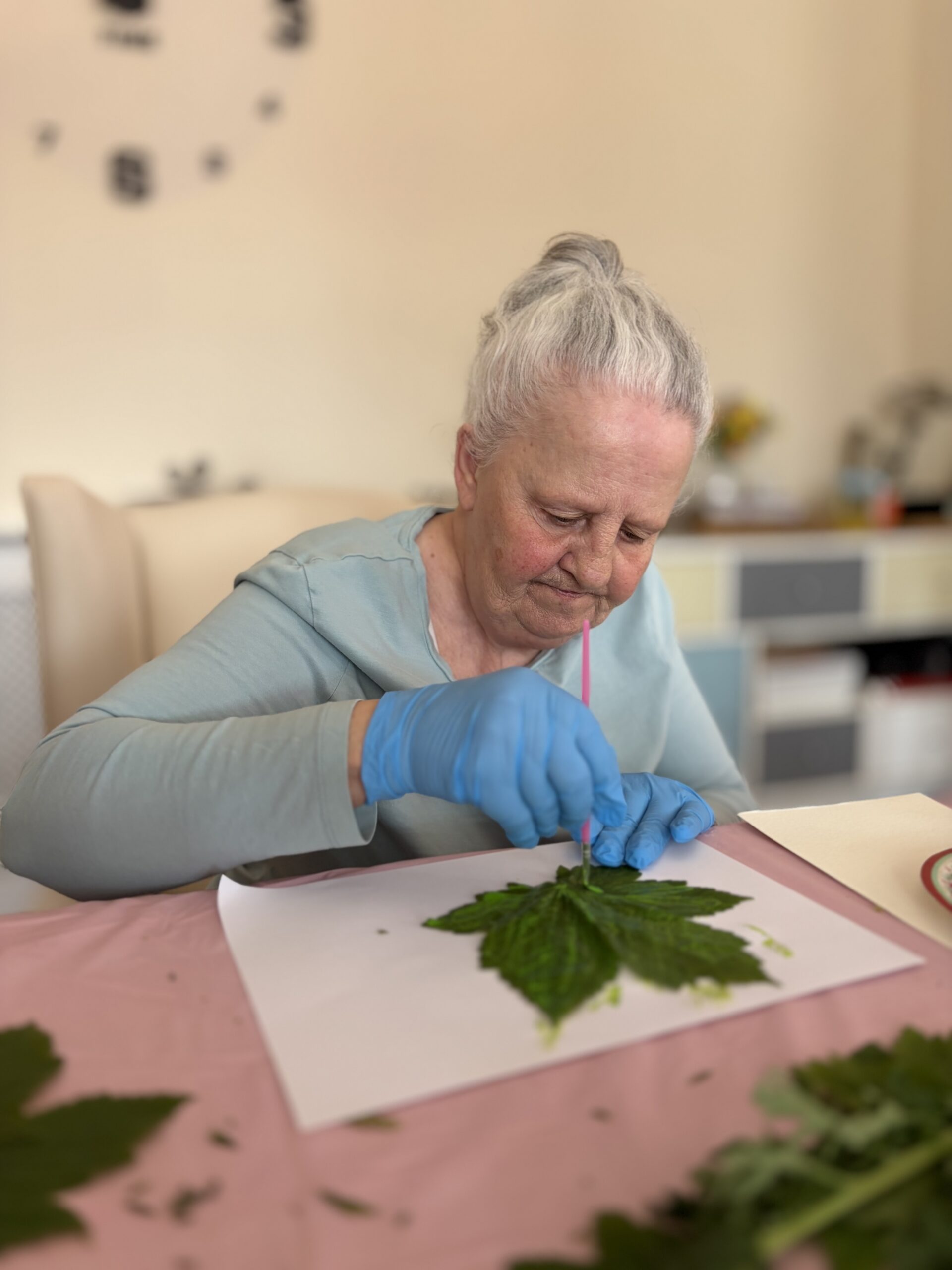 Female resident seated using yellow paint to create her leaf artwork