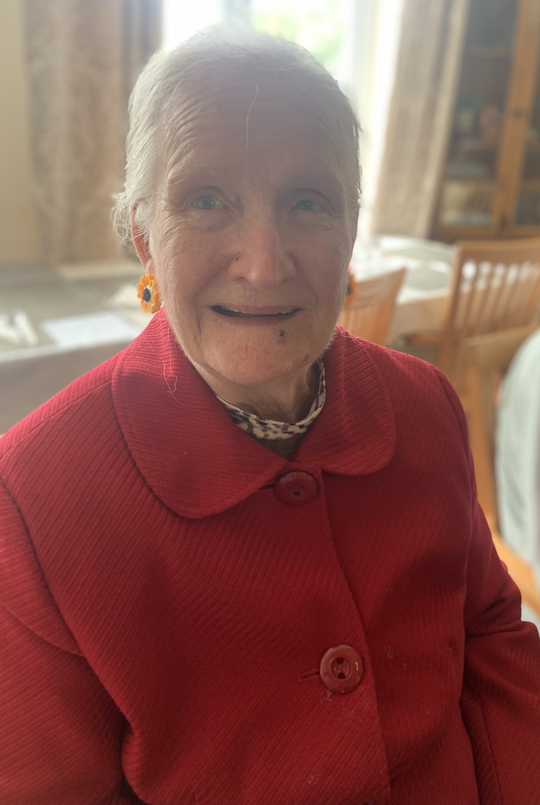 Female resident wearing a red jacket and colourful earrings smiling for the camera