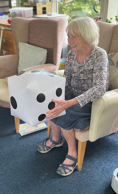 Jean seated holding a large blow-up dice smiling
