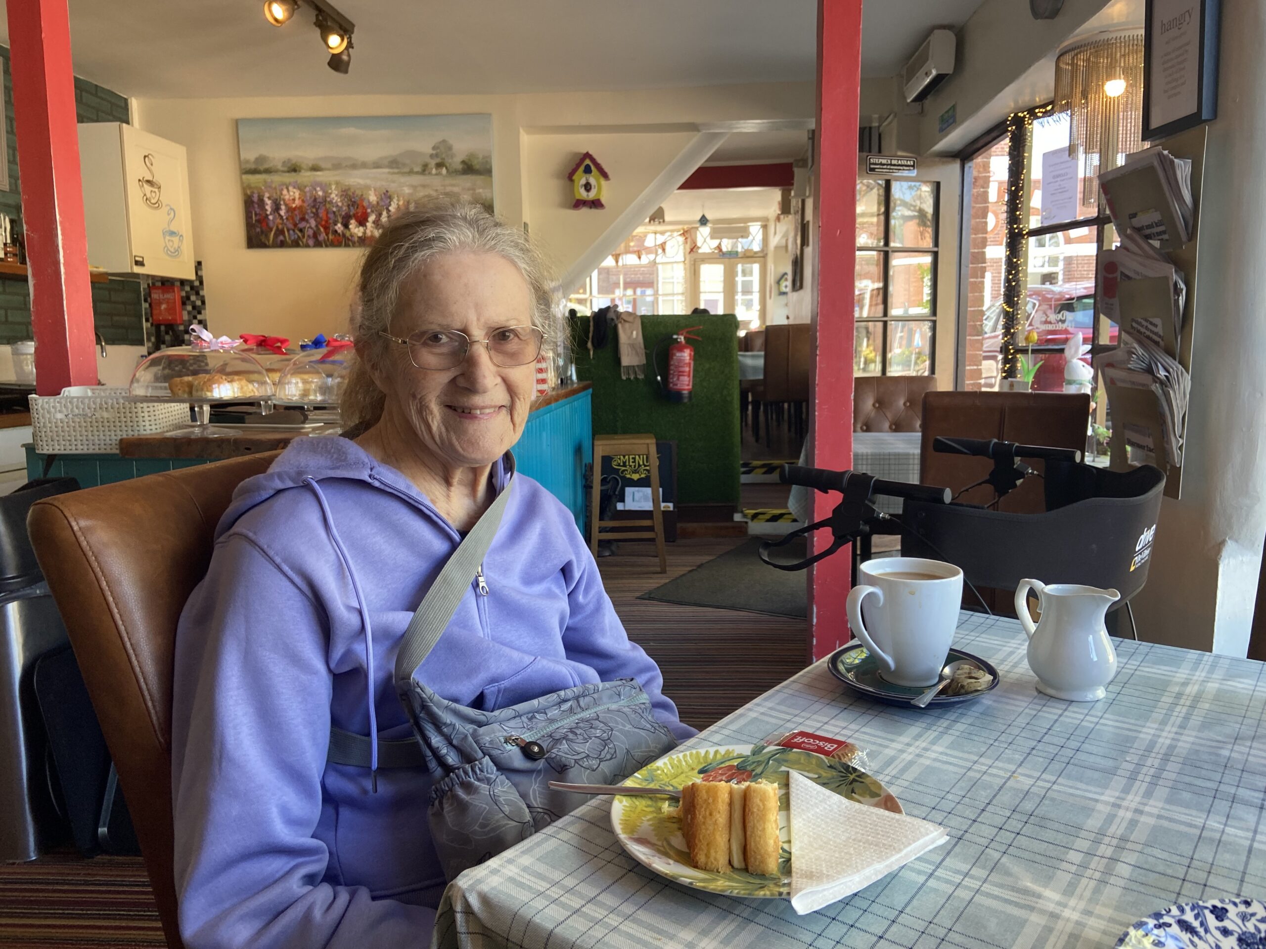 Lesley seated in a teashop cafe with a piece of lemon drizzle cake scaled