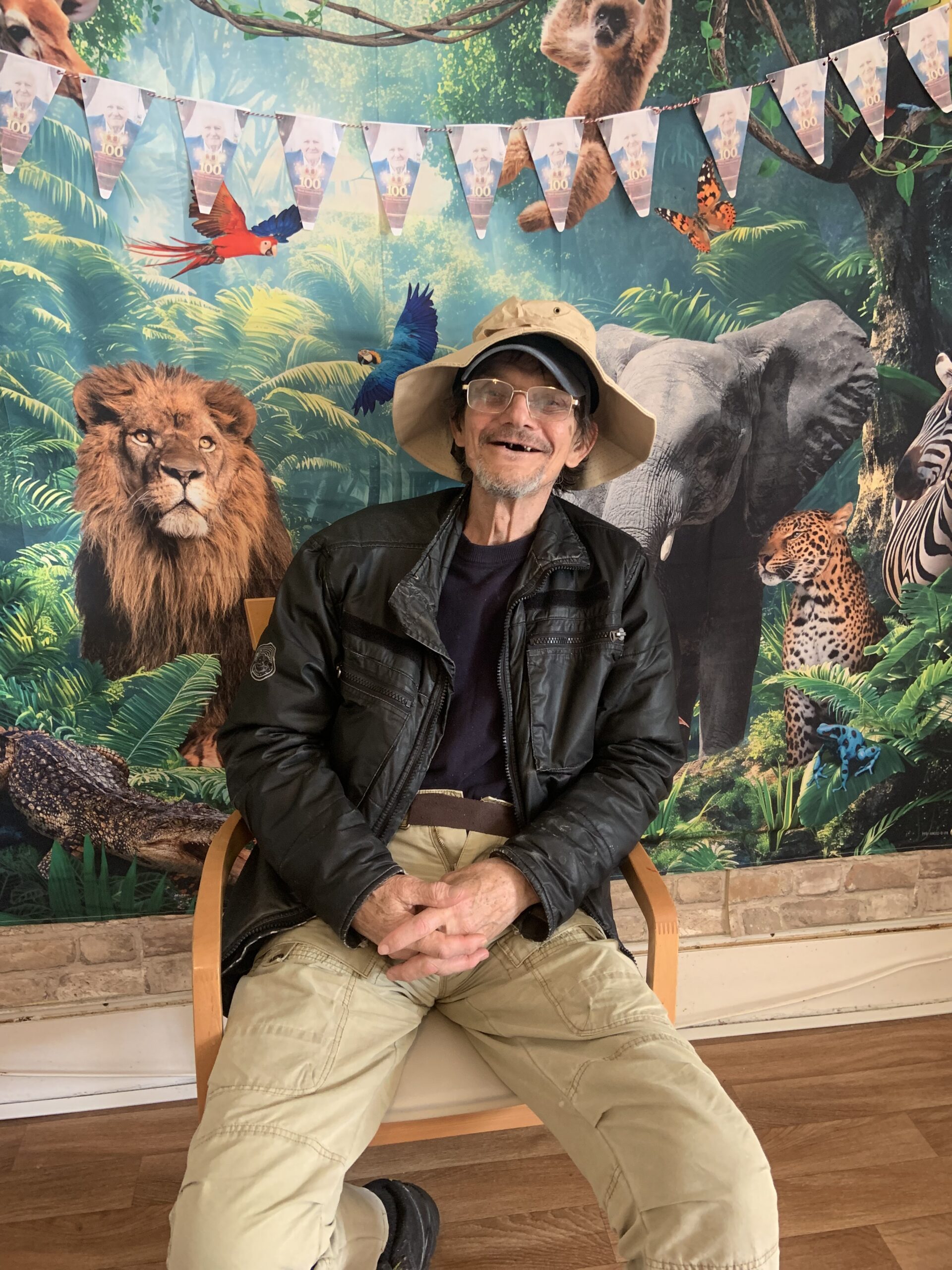 Male resident in a safari hat seated in front of jungle back drop