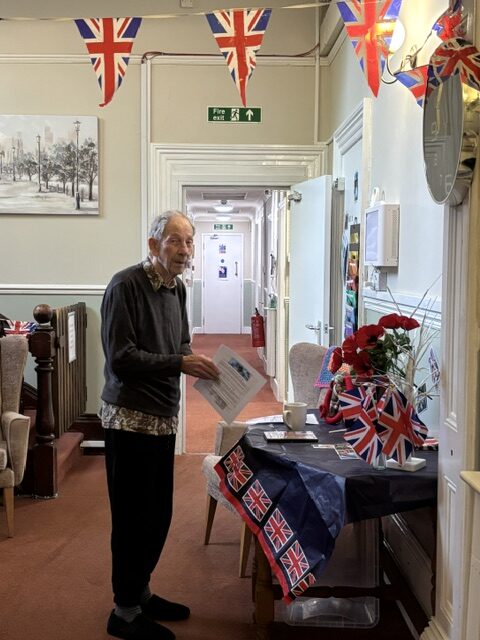 Male resident standing at a table of WW2 memorabilia smiling