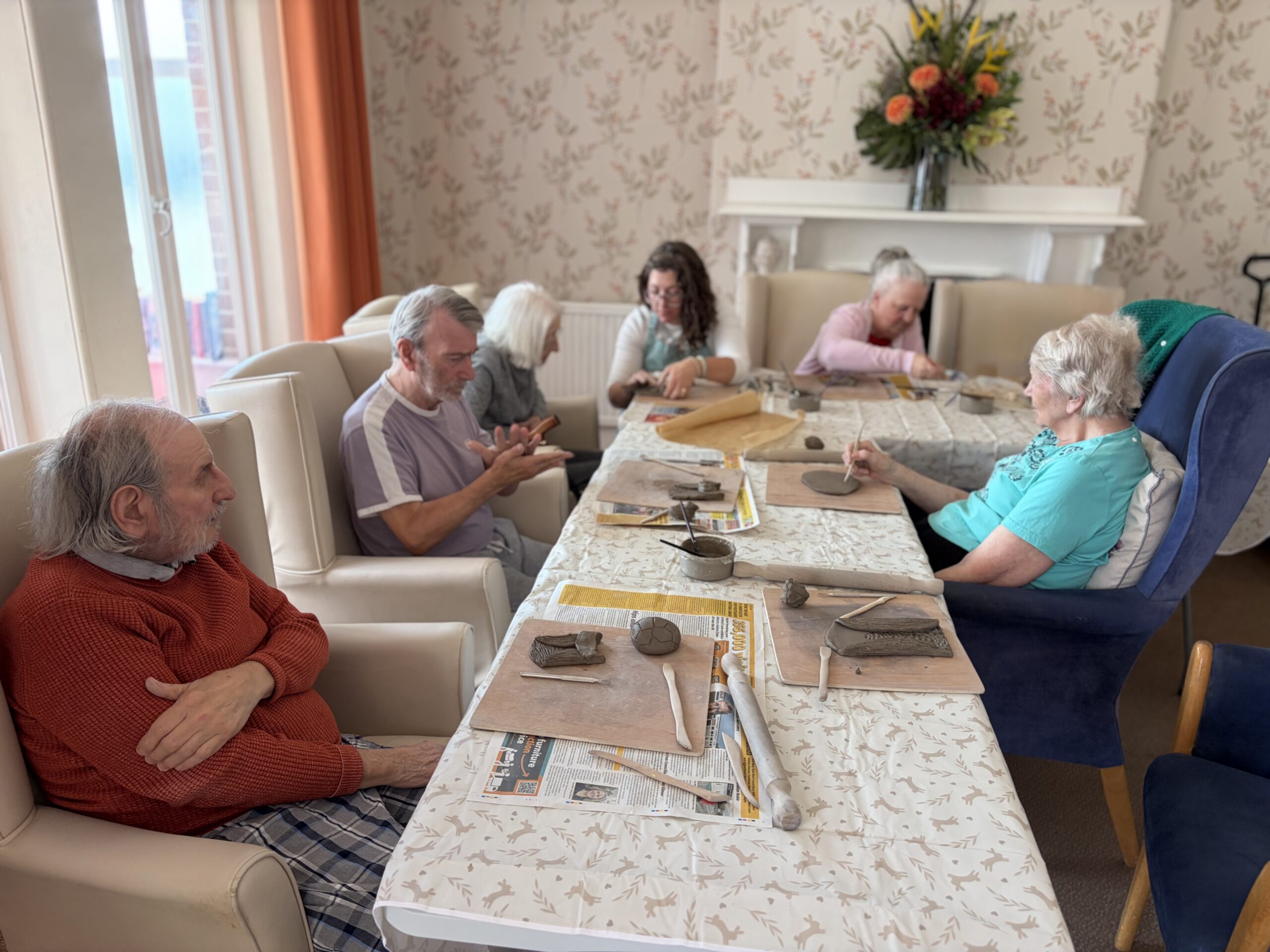 Residents and Rachael seated around an l=shaped tables with clay and tools at the ready