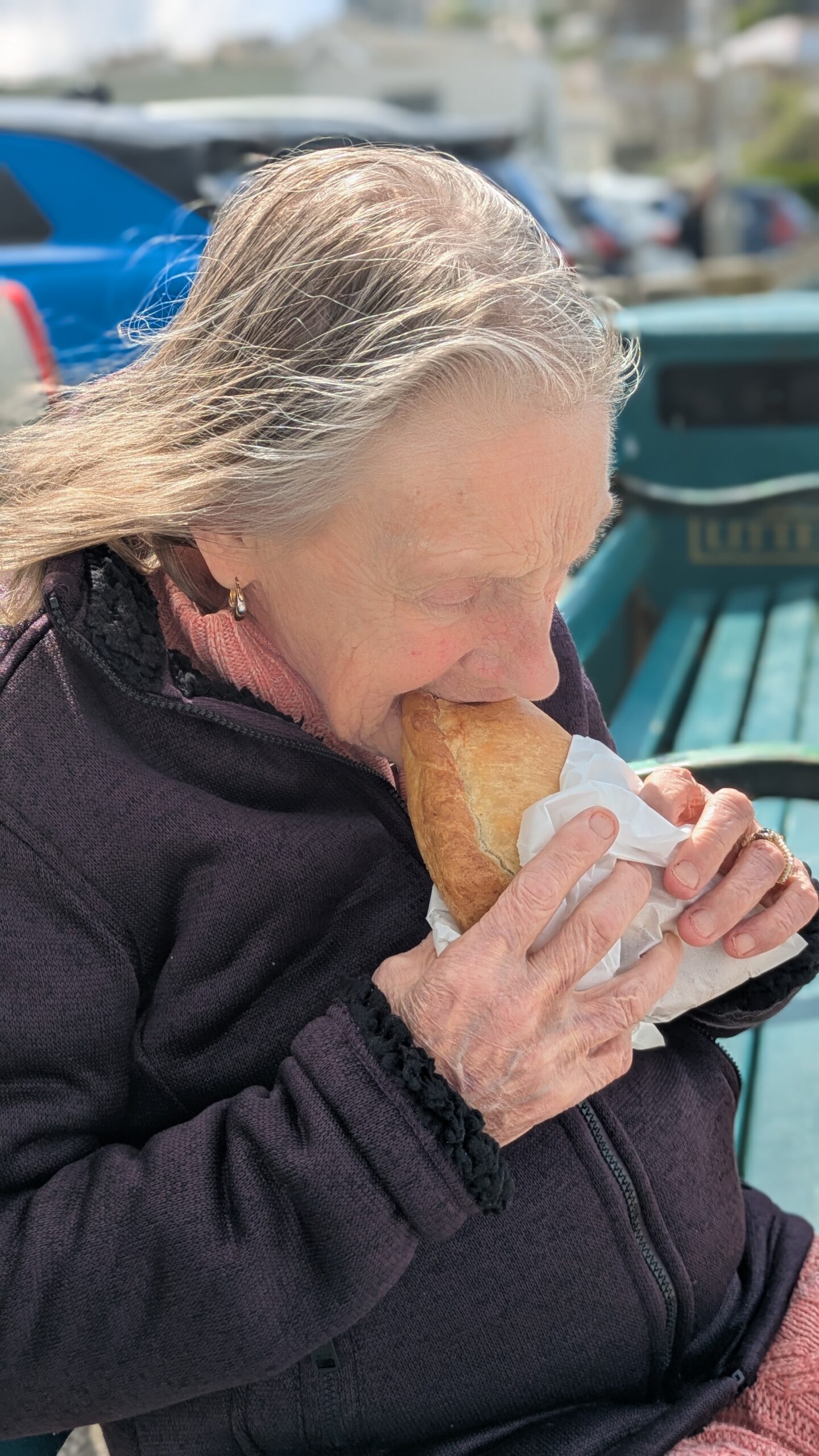 Thelma seated on a bench eating a Cornish pasty