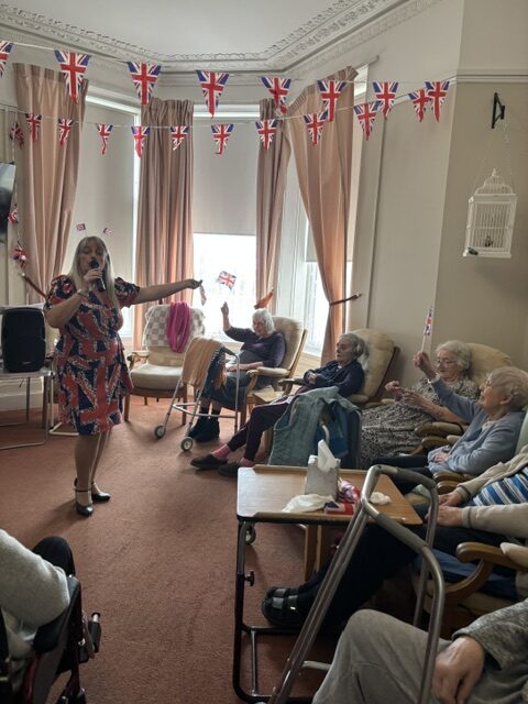 Zara singing to seated residents waving Union Jacks