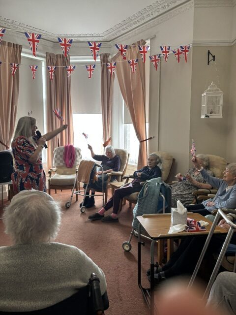 Zara singing to seated residents waving their flags